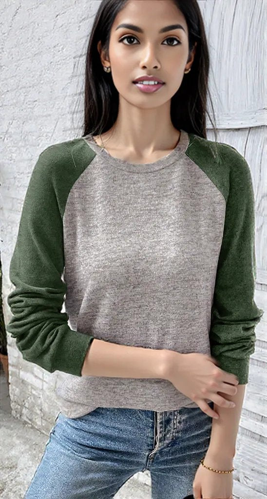 Woman wearing a gray and green long-sleeve shirt against a light stone wall.