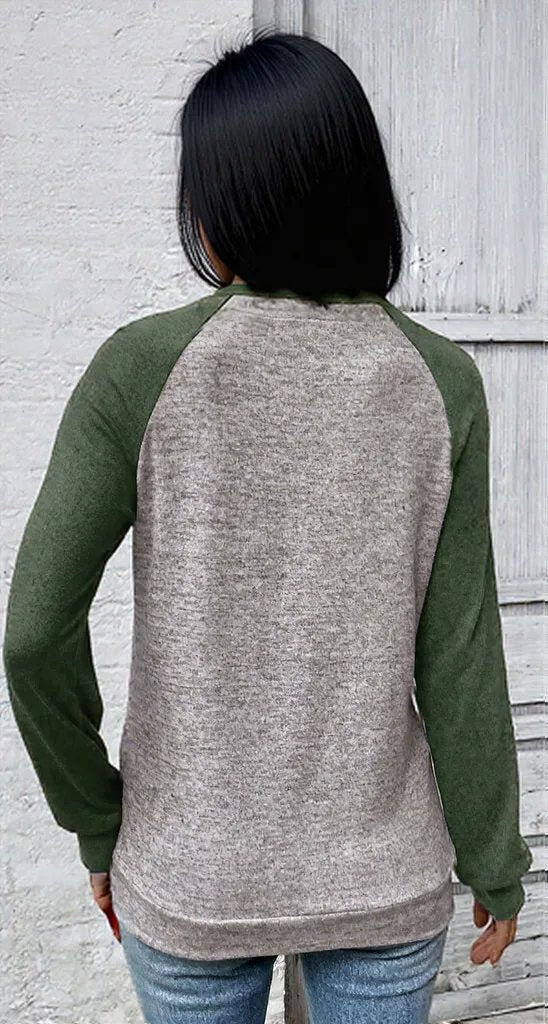 Person wearing a gray and green long-sleeve shirt against a light gray wall.