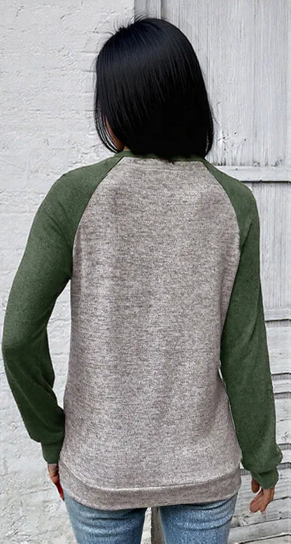 Person wearing a gray and green long-sleeve shirt against a light gray wall.